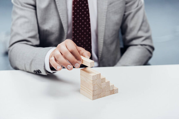 selective focus of man putting wooden brick on top of wooden blocks symbolizing career ladder