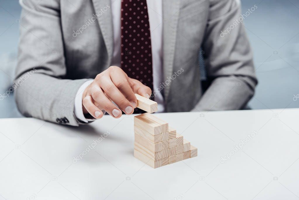 selective focus of man putting wooden brick on top of wooden blocks symbolizing career ladder