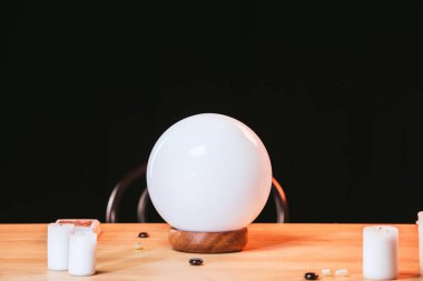 selective focus of crystal ball near candles on wooden table isolated on black  clipart