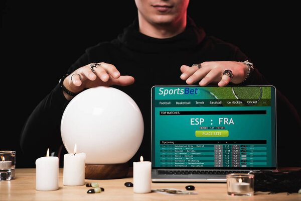 cropped view of oracle near laptop with sports bet website on screen isolated on black 