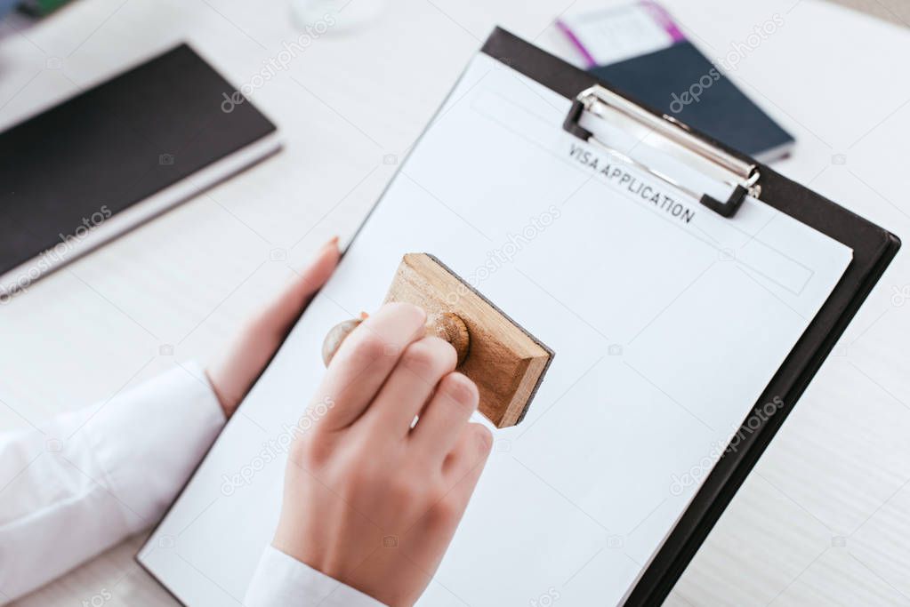 selective focus of female lawyer with stamp in hand holding clipboard with visa application lettering on document 