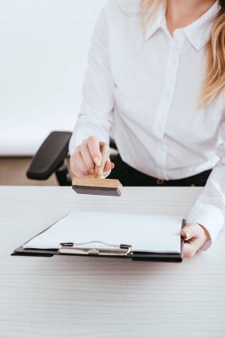 selective focus of  female lawyer holding clipboard and stamp in hands clipart