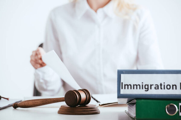 selective focus of gavel near folders with immigration law lettering with woman on background isolated on white