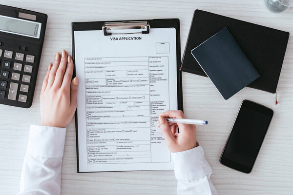 вид сверху на женщину, держащую ручку рядом с документом с визовой надписью рядом со смартфоном с пустым экраном
 