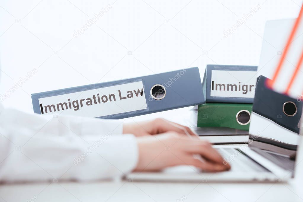 selective focus of folders with immigration law lettering near woman using laptop isolated on white