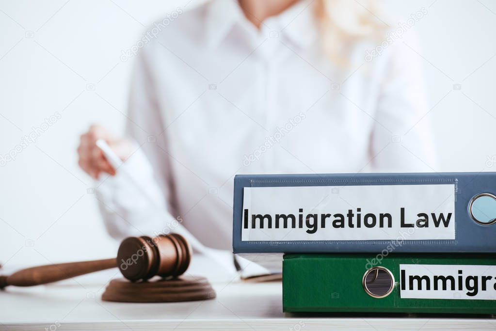 selective focus of folders with immigration law lettering near gavel with woman on background isolated on white