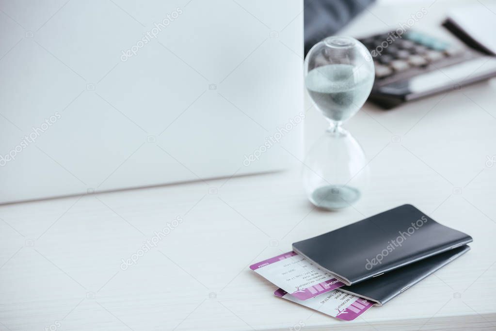 selective focus of sand running in houglass near passports with tickets 