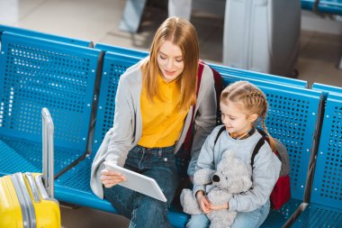 Dijital tablet tutarak ve havaalanında kızıyla oturan anne havai görünümü 