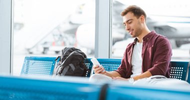akıllı telefon tutarak ve bekleme salonunda beklerken gülümseyen neşeli adam
