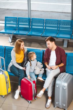 overhead view of father talking with daughter near suitcases and wife in departure lounge clipart