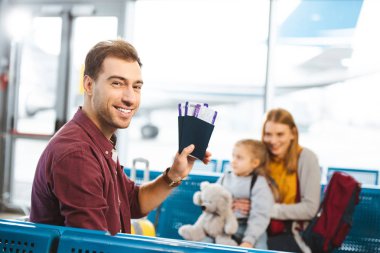 seçici odak pasaportlar uçak bileti ile karısı ve kızı ile arka planda tutarak gülümseyen yakışıklı adamın 