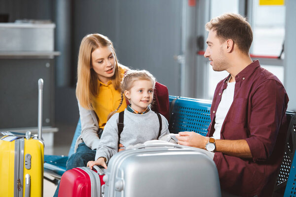 attractive mother talking with daughter near suitcases and husband in departure lounge
