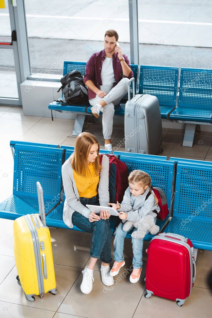 overhead view of mother holding digital tablet and sitting in waiting hall with daughter 
