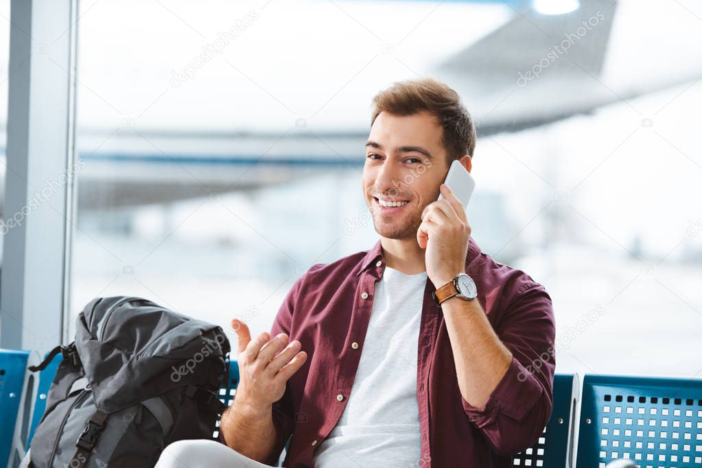 smiling man talking on smartphone while waiting in waiting hall