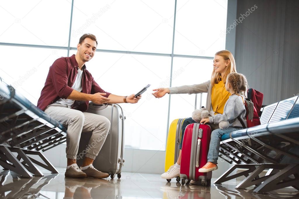 happy father giving passports with air tickets to wife near daughter in airport 