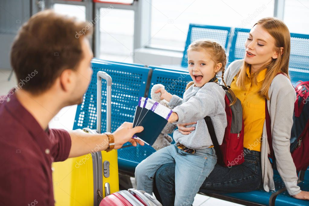 selective focus of excited daughter smiling with mother near father with passports with air tickets 