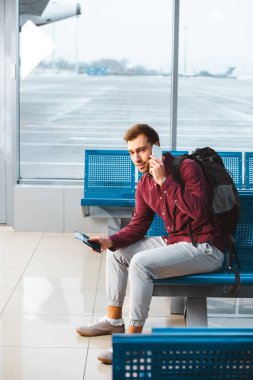 sırt çantası ile bekleme salonunda otururken Smartphone'da konuşan yakışıklı adam
