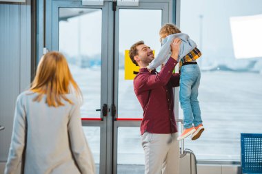 selective focus of happy father holding in arms daughter near wife in airport  clipart