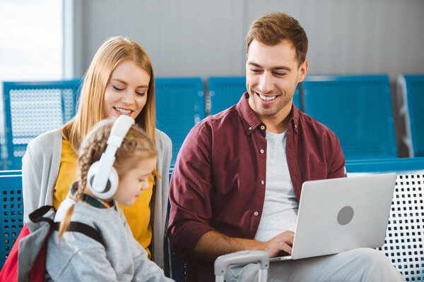 selective focus of woman sitting near husband with laptop and smiling near daughter in headphones 