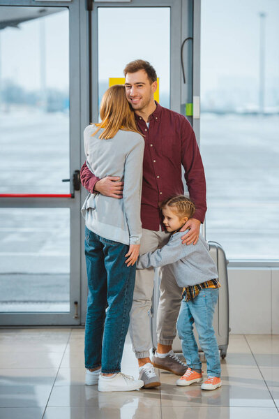 handsome man hugging wife and daughter in airport 
