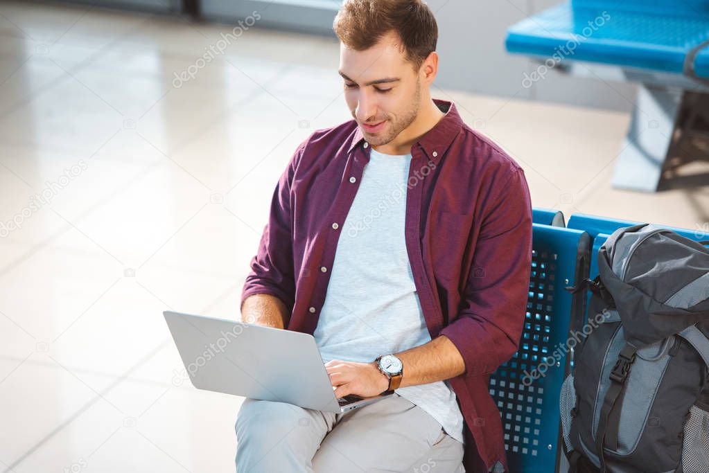 overhead view of cheerful man using laptop while sitting in departure lounge 