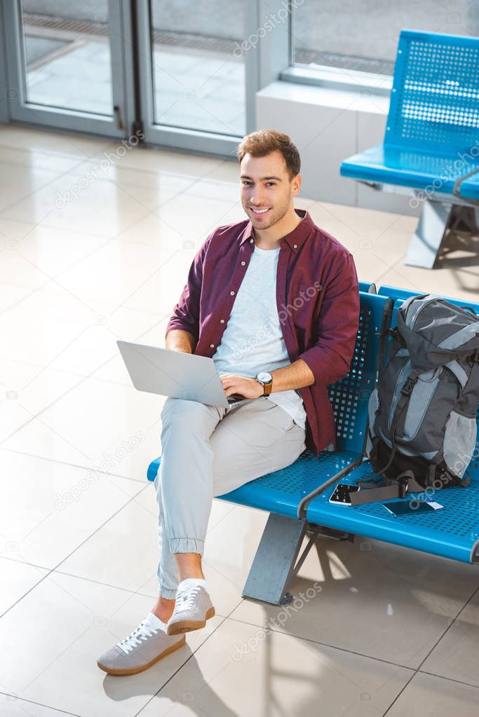 overhead view of smiling man using laptop while waiting in departure lounge