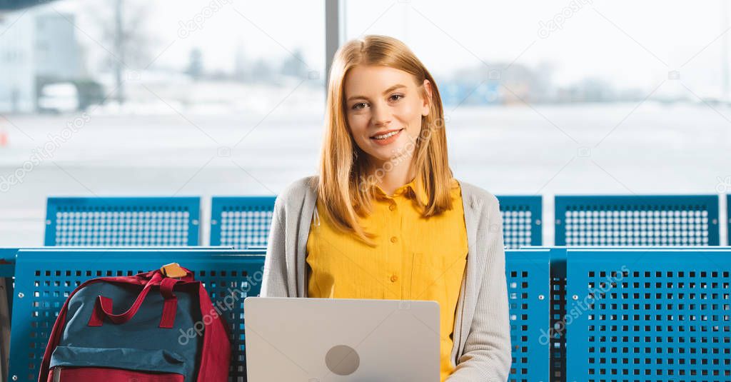 attractive woman smiling while using laptop in departure lounge