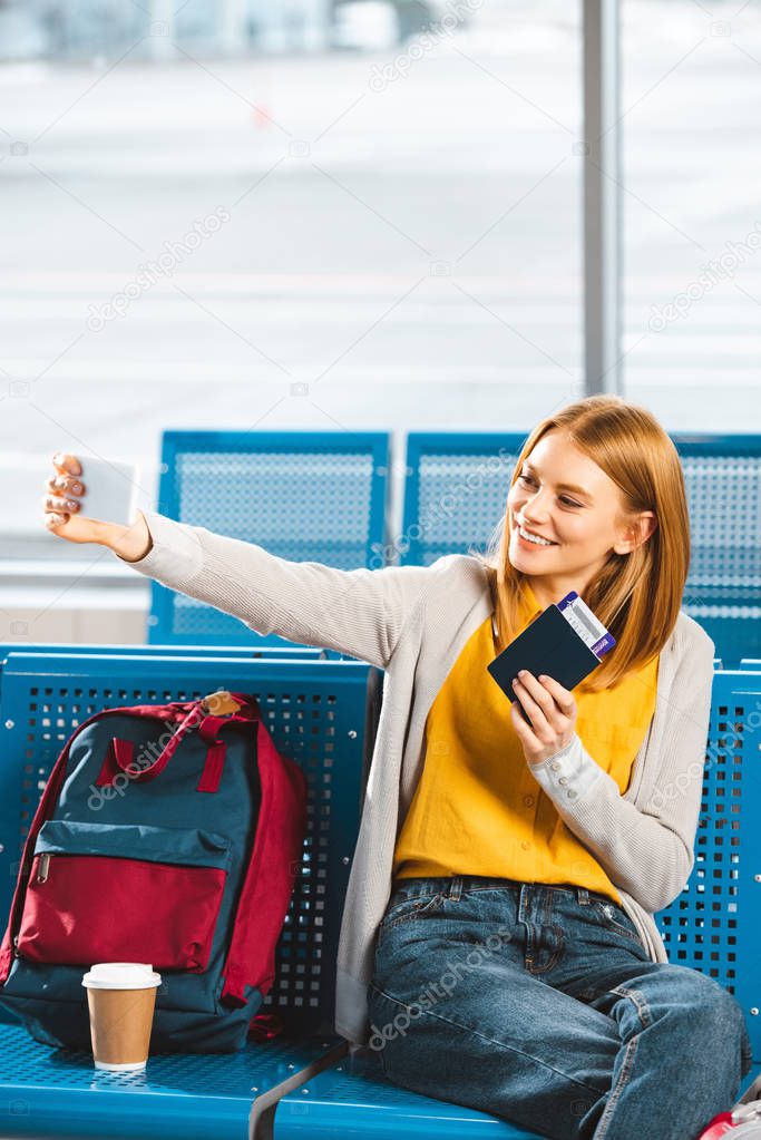 attractive woman taking selfie with passport and air ticket in waiting hall
