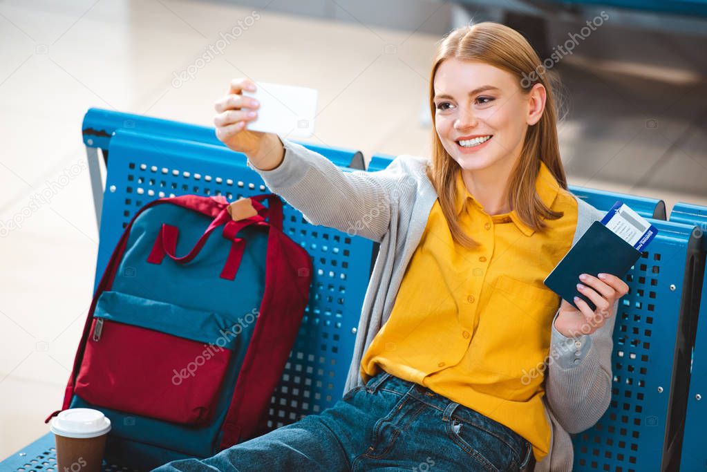 selective focus of cheerful woman taking selfie in airport 