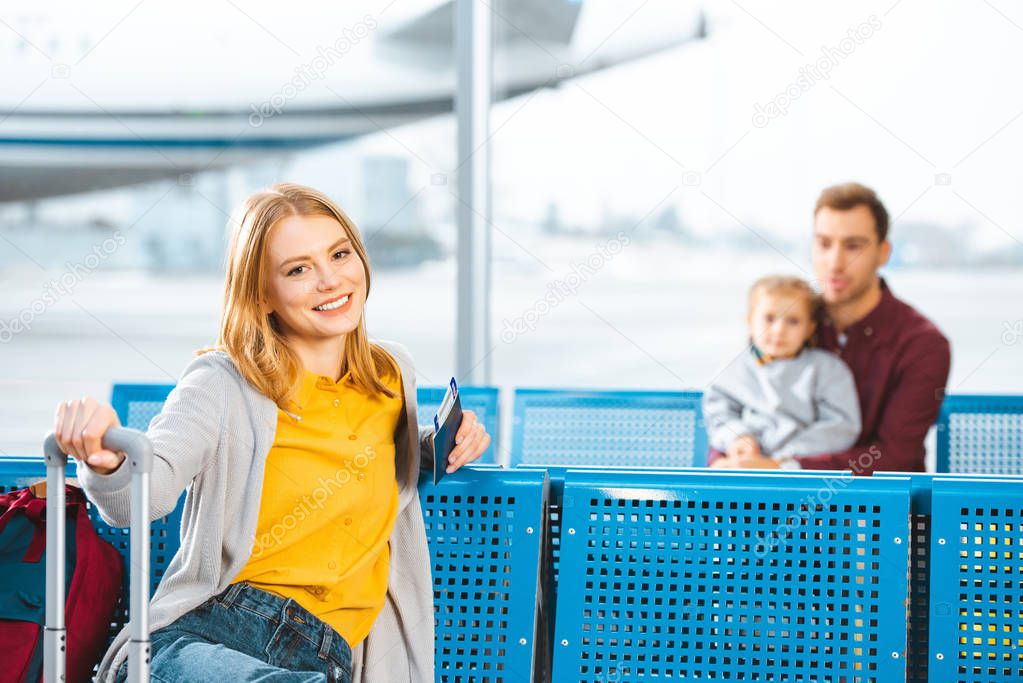 selective focus of woman holding passport with air ticket and smiling with people on background 
