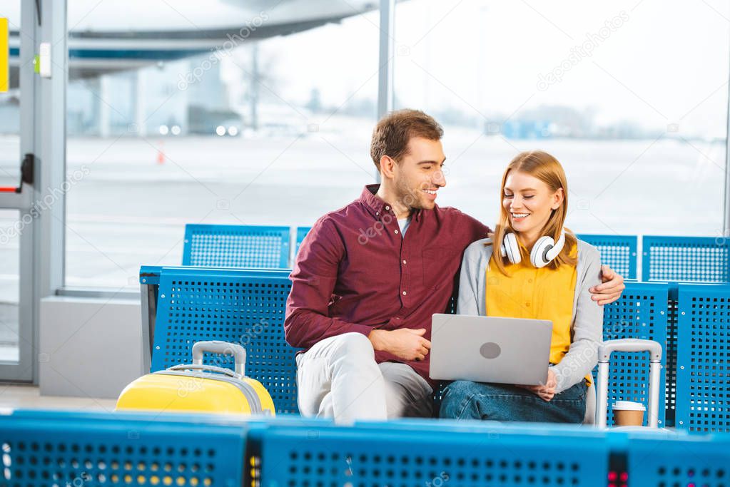 happy man looking at girlfriend with laptop in airport