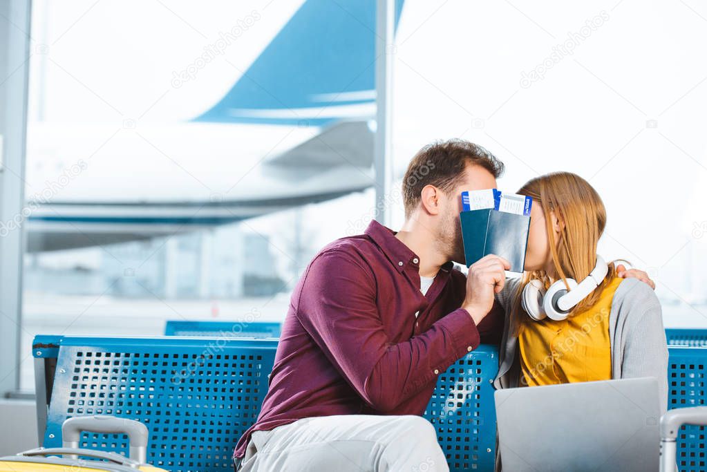 boyfriend and girlfriend covering faces with passports in airport lounge