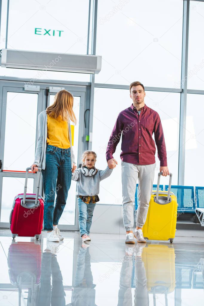 happy wife and husband holding hands with cute daughter in departure lounge