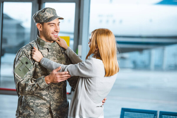 happy woman hugging boyfriend in military uniform in airport 