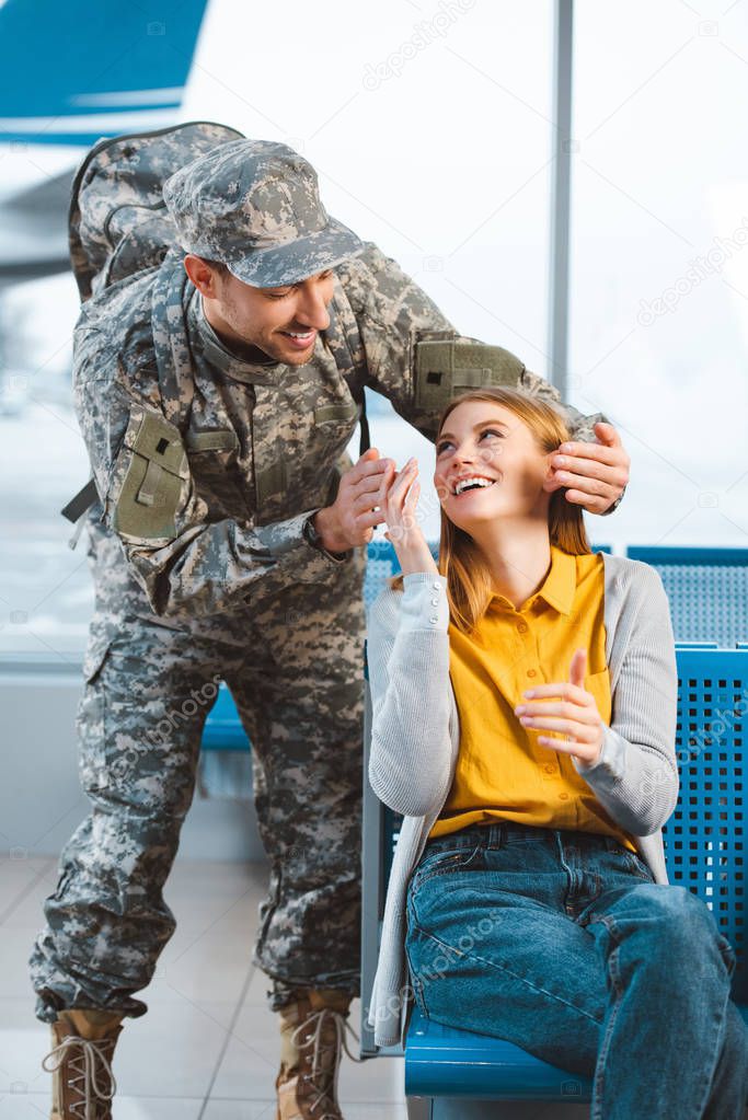 cheerful veteran looking at surprised girlfriend in airport 