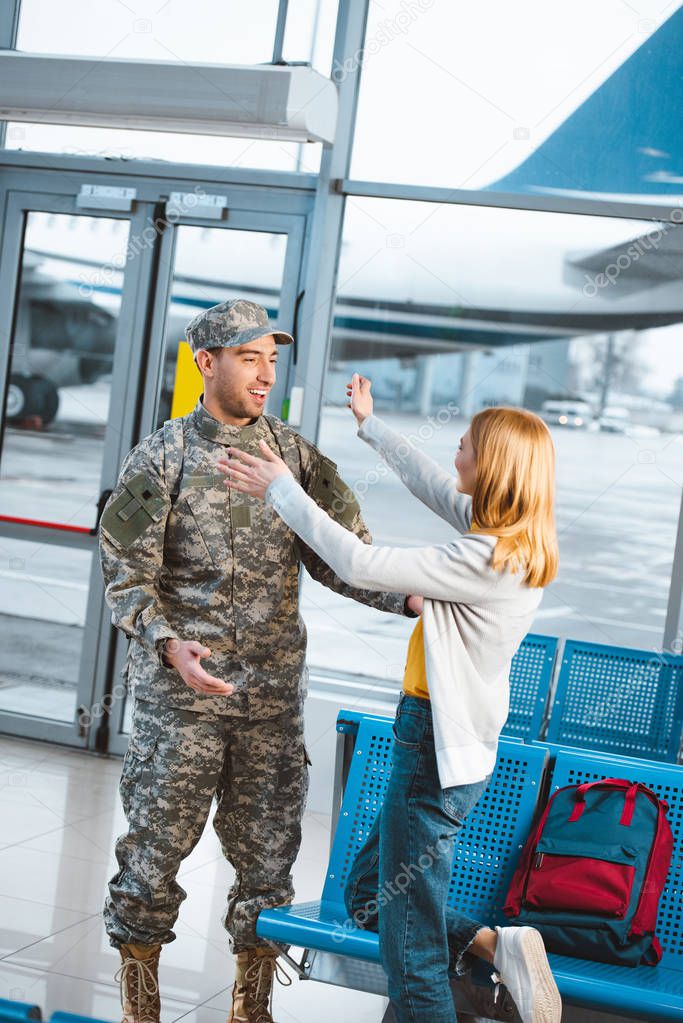 happy woman looking at boyfriend in military uniform and standing with opened arms 