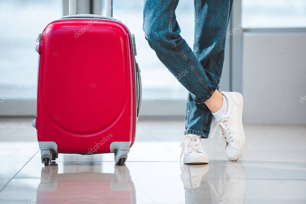 cropped view of woman standing with suitcase with crossed legs in airport 