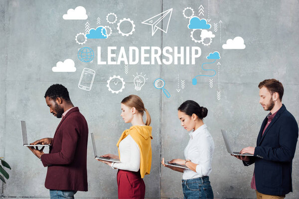 мультиэтнические случайные предприниматели используют ноутбуки, стоя в очереди в зале ожидания с иллюстрацией лидерства на стене
