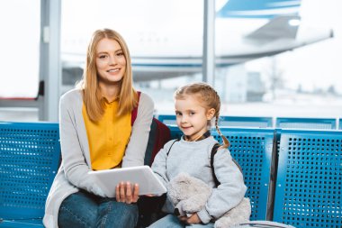 Dijital tablet holding ve havaalanında kızıyla oturmuş güzel anne 