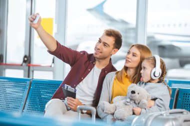 Selfie alma ve karısıyla kızını dil hava alanında gösterilen yakınındaki gülümseyen neşeli baba 