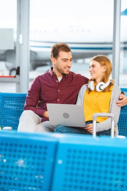 gülümseyen çift birbirine yakın havaalanı içinde laptop bakarak