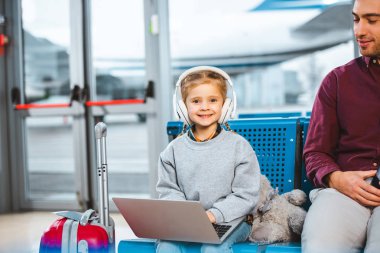 gülümseyen çocuk havaalanında baba yakınındaki laptop kullanırken kulaklık müzik dinleme 