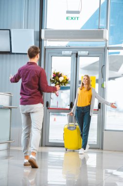 back view of boyfriend with flowers meeting beautiful girlfriend with suitcase in airport  clipart