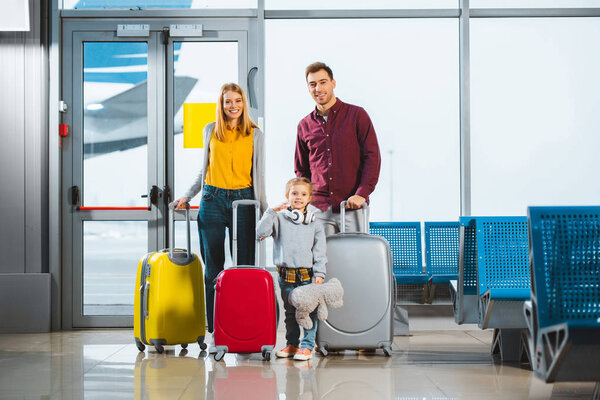 cheerful family standing with luggage in waiting hall of airport
