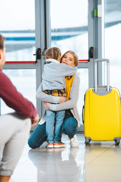 mother hugging daughter near luggage in airport 