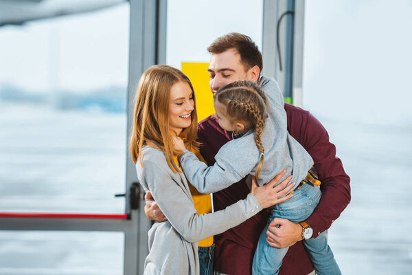 cheerful family smiling while hugging in airport 