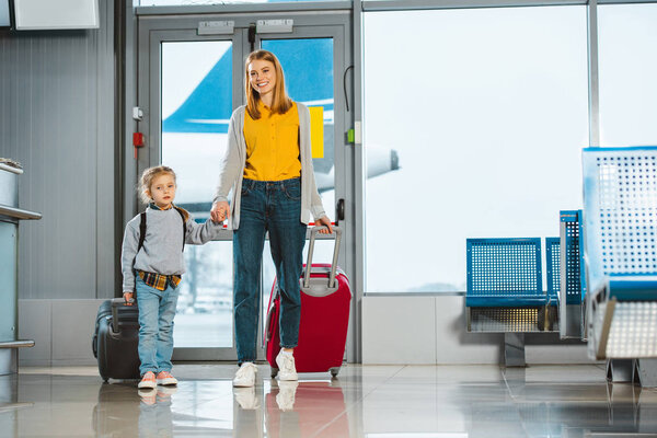 cheerful mother holding hands with cute daughter in airport 