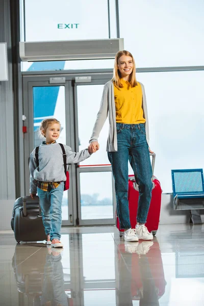 有吸引力的母亲手与可爱的女儿 而走与行李箱在机场 — 图库照片