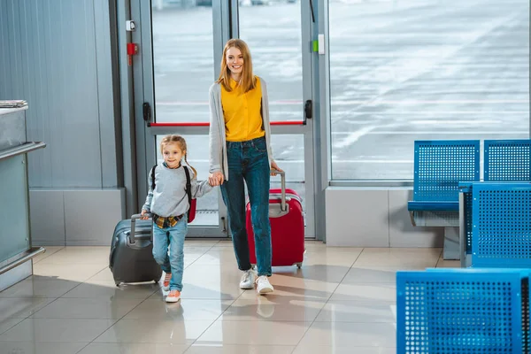 neşeli anne havaalanında bavul ile yürürken sevimli ile elele