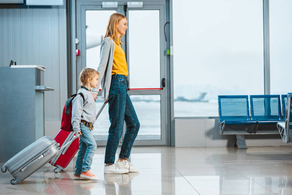 mother and daughter holding hands and walking with baggage in airport 